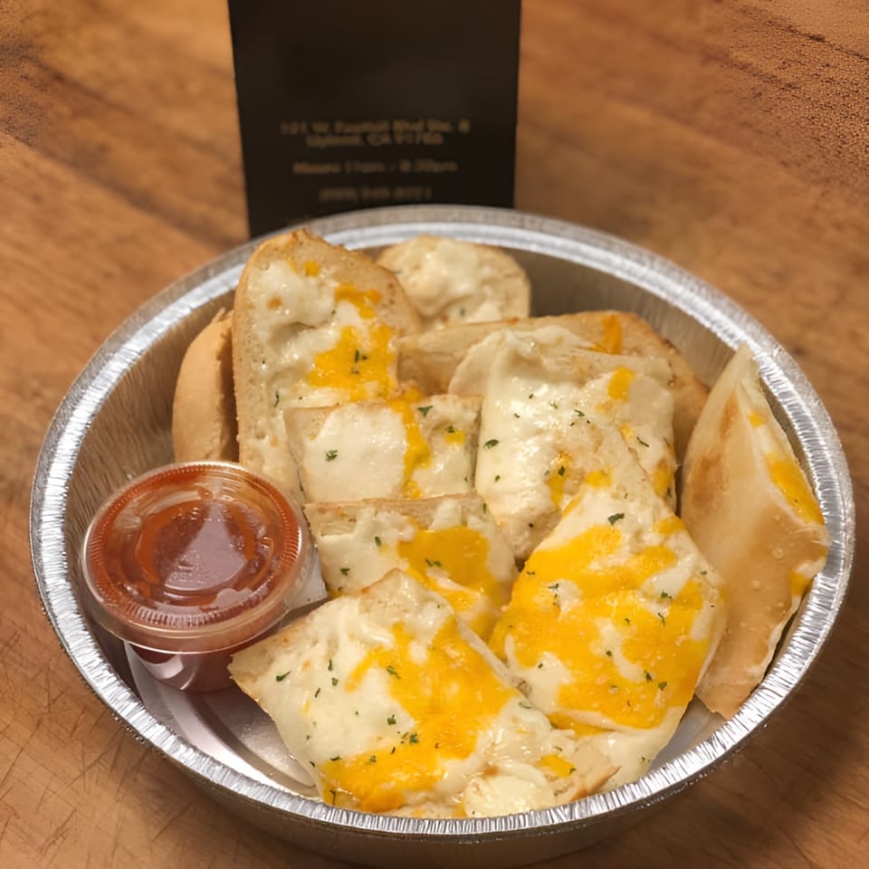 Cheesy garlic bread with melted mozzarella and cheddar, served in a foil pan with a side of marinara.